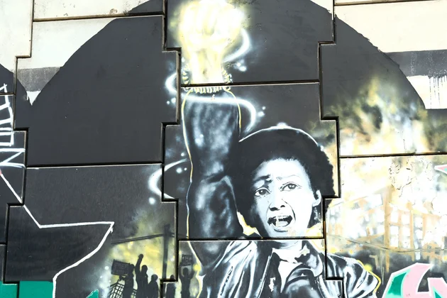 Une peinture murale urbaine représentant une personne qui proteste avec le poing levé et illuminé, symbole de lutte et de libération.