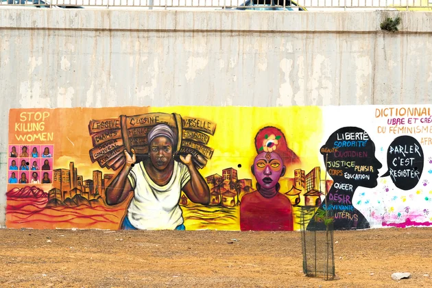Une fresque murale féministe colorée peinte sur un grand mur en béton à Dakar, illustrant des messages et des portraits de femmes africaines engagées.