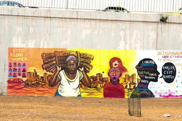Une fresque murale féministe colorée peinte sur un grand mur en béton à Dakar, illustrant des messages et des portraits de femmes africaines engagées.