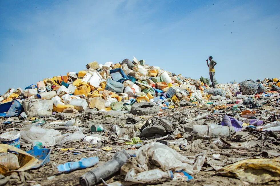 Photographie d'un énorme tas de déchets plastiques, observé par un homme 