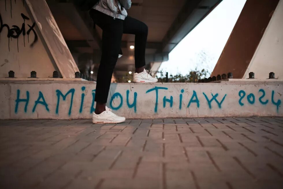 jeune portant des baskets posant devant un banc public tagué